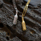 Gold and silver bottle of beer pendants on chains against a textured dark background