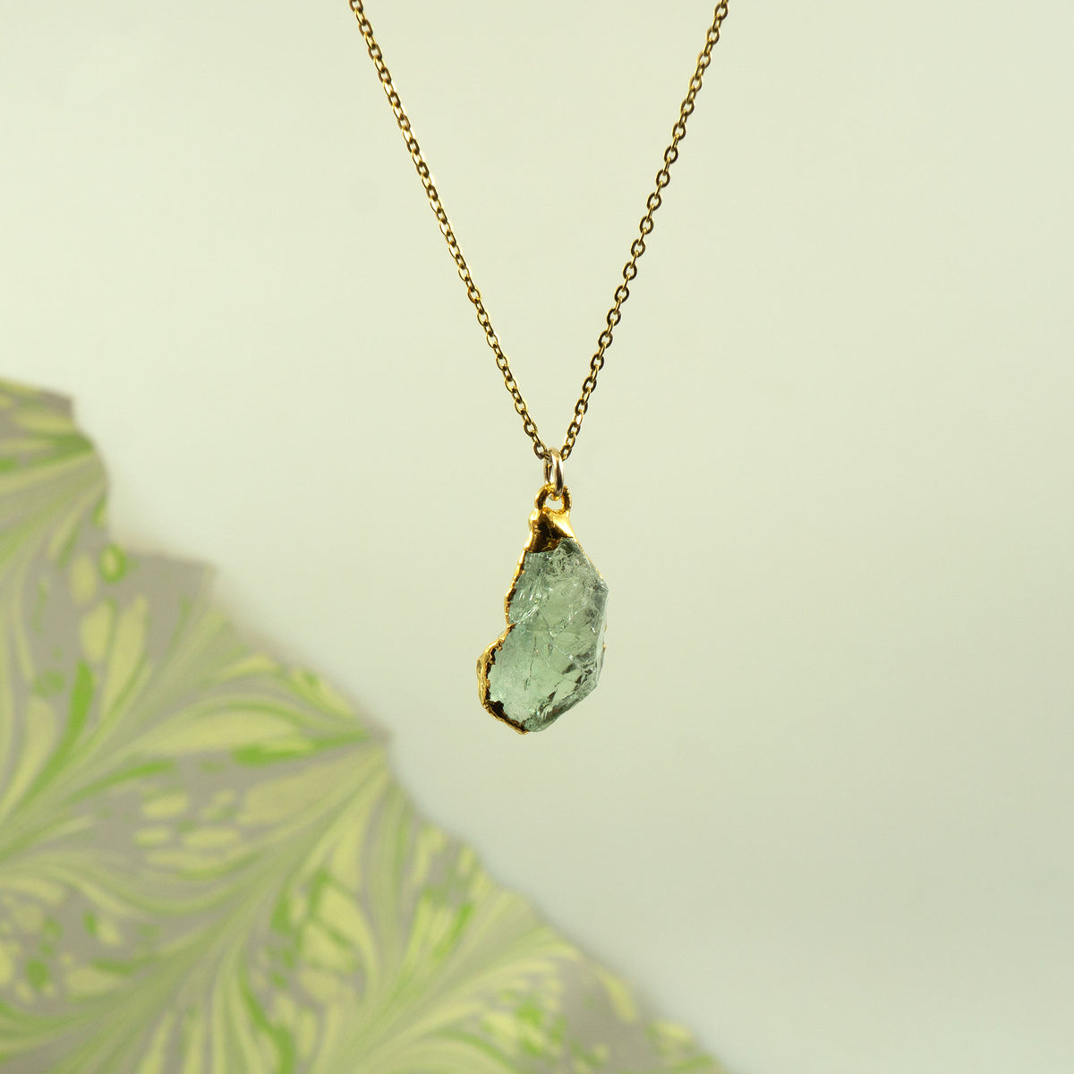 A gold chain necklace with a raw, unpolished Green Amethyst gemstone pendant