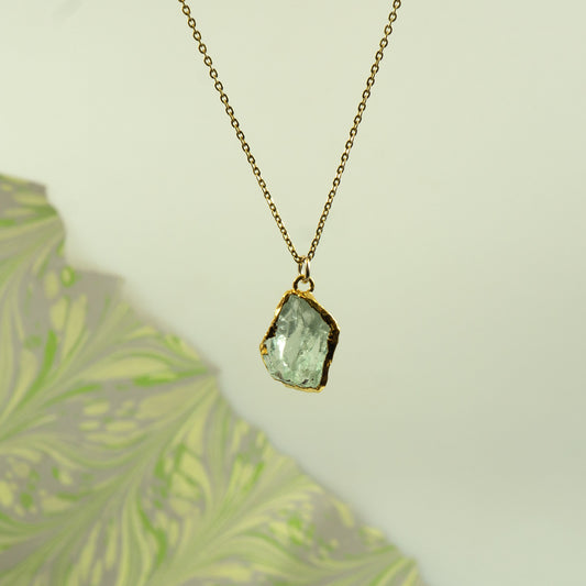 A gold chain necklace with a raw, irregular-cut Green Amethyst gemstone pendant