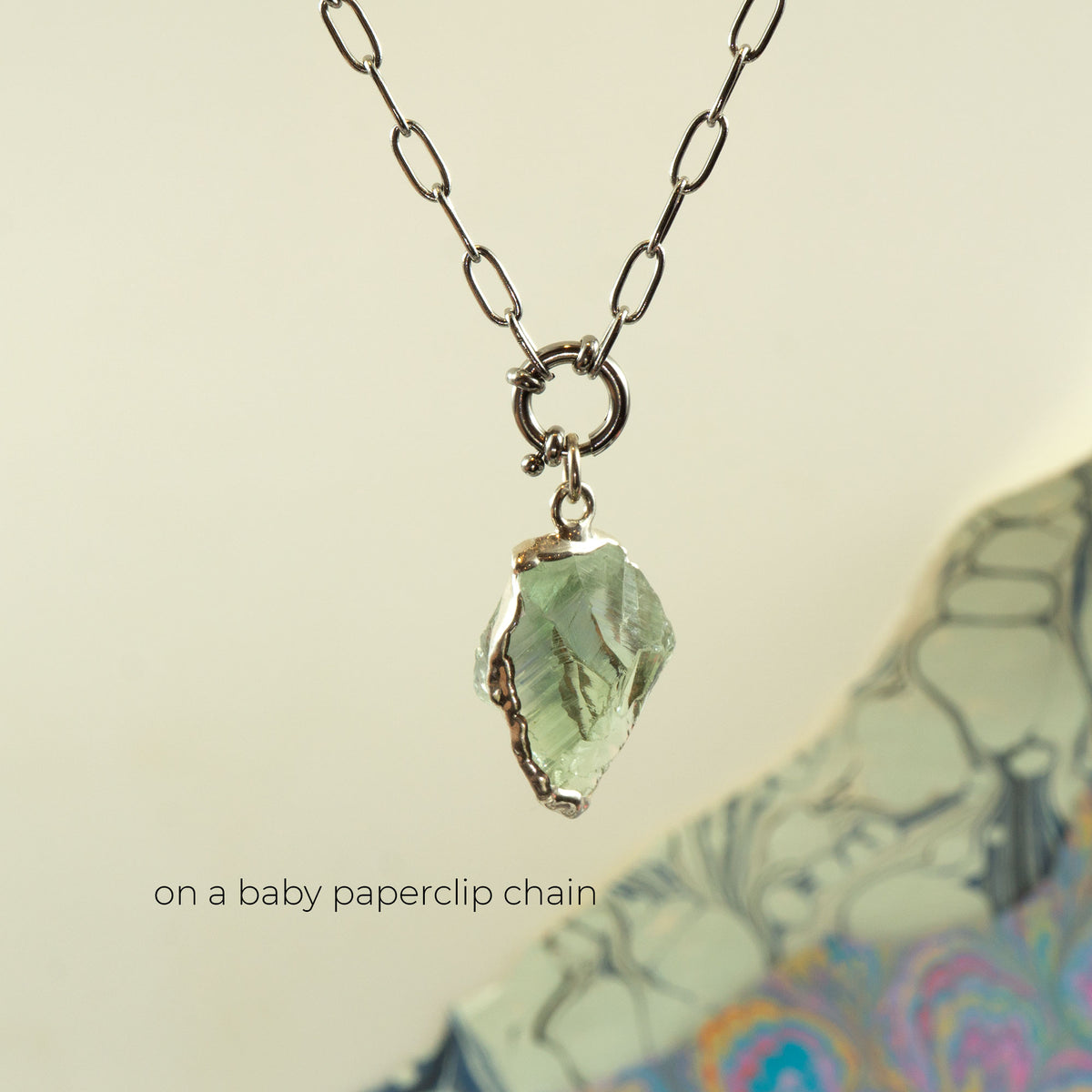 A silver paperclip chain necklace with a raw, irregular light Green Amethyst gemstone pendant
