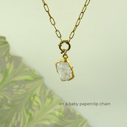 A gold paperclip chain necklace with a raw, rough-cut clear Herkimer Diamond pendant in a gold bezel setting
