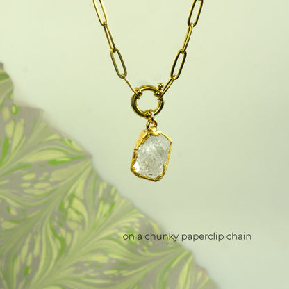 A gold necklace with a chunky paperclip chain and a raw, rough-cut clear raw Herkimer Diamond pendant