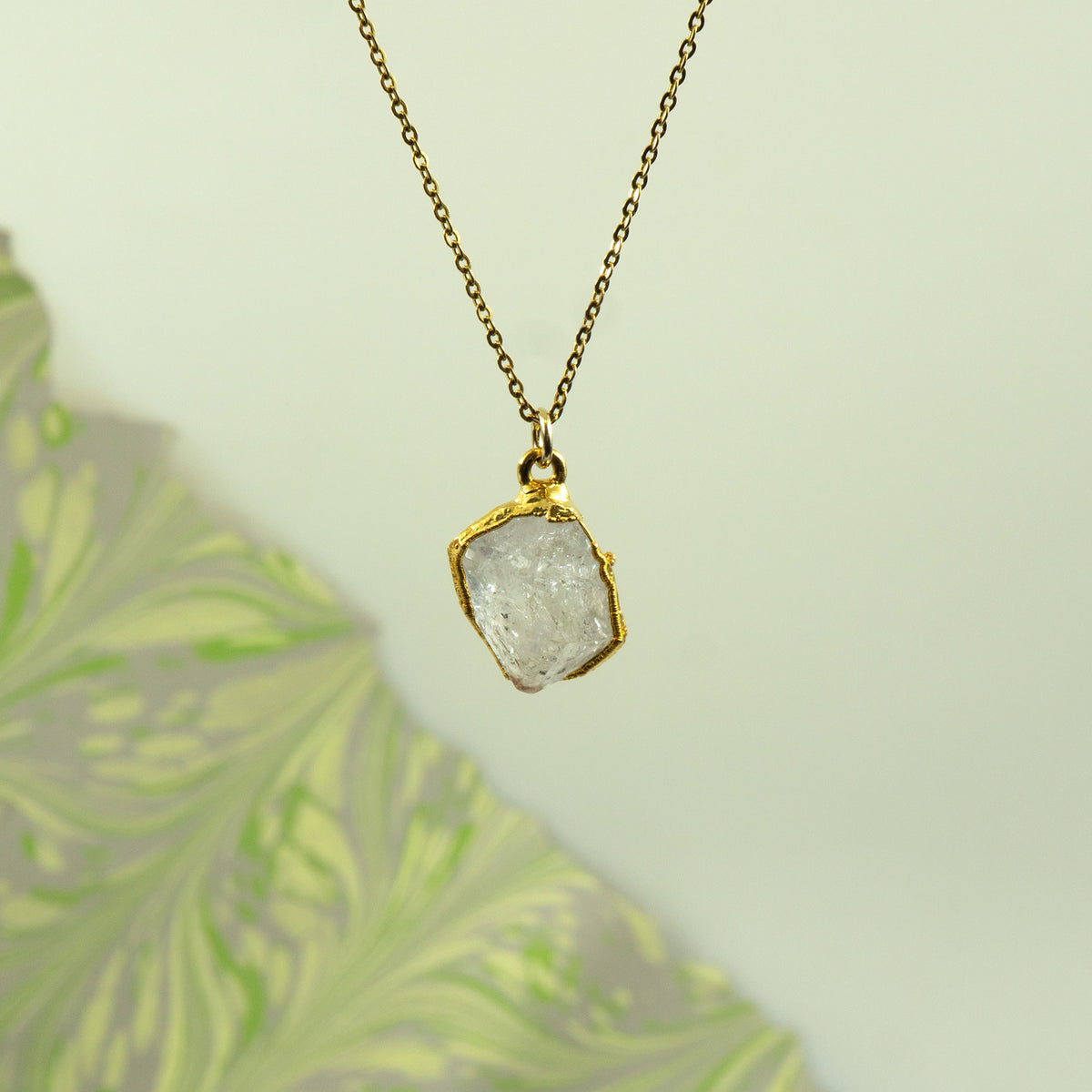 A gold chain necklace with a raw, irregular-cut clear Herkimer Diamond pendant in a gold bezel setting