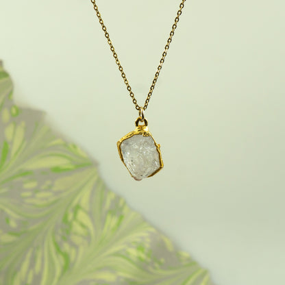 A gold chain necklace with a raw, irregular-cut clear Herkimer Diamond pendant in a gold bezel setting