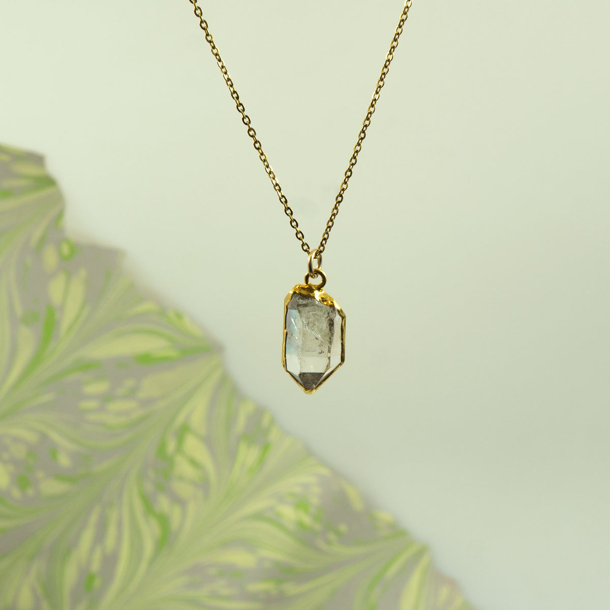 A gold chain necklace with a faceted clear Herkimer Diamond pendant