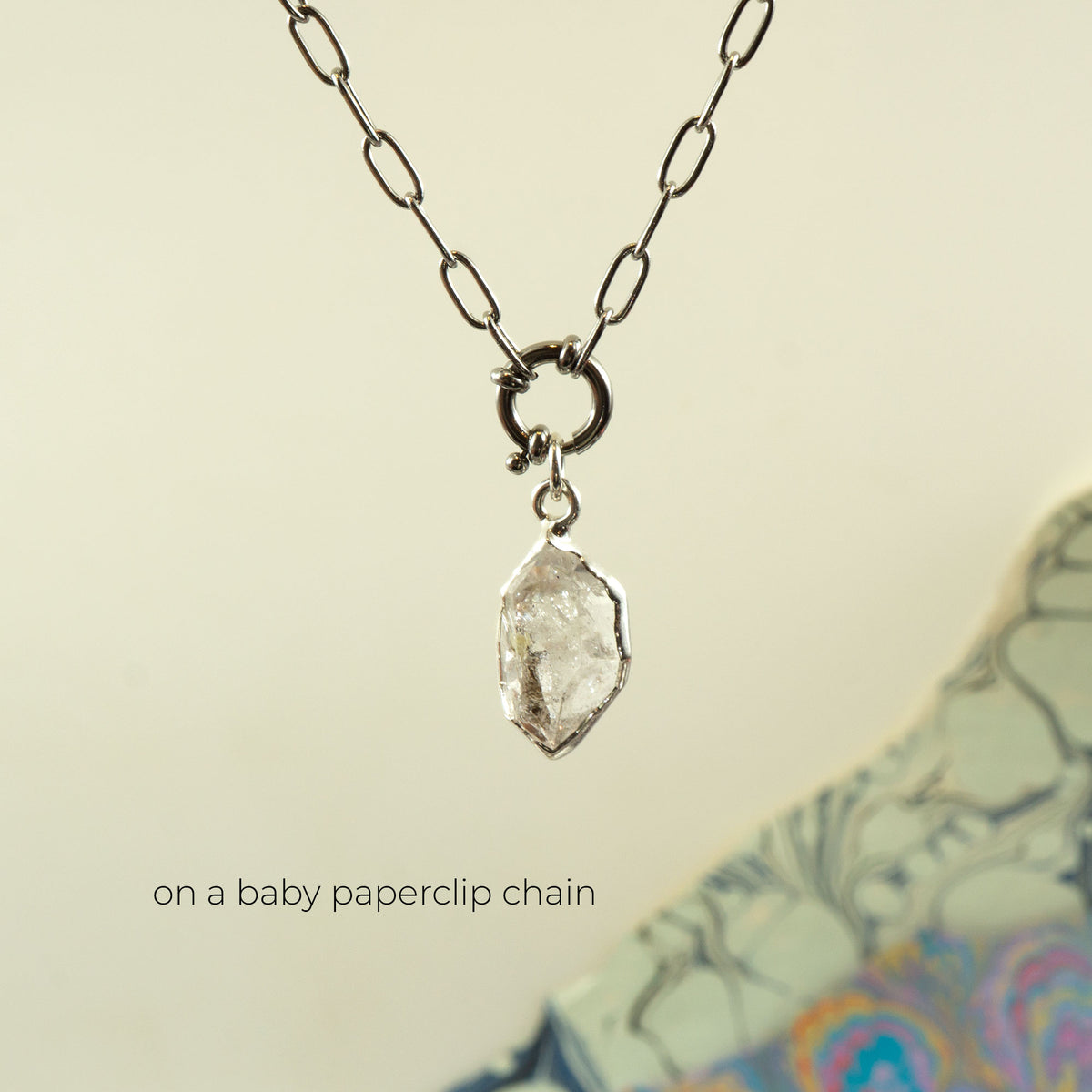 A silver paperclip chain necklace holding a rough, clear faceted Herkimer Diamond pendant.