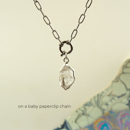 A silver paperclip chain necklace holding a rough, clear faceted Herkimer Diamond pendant.