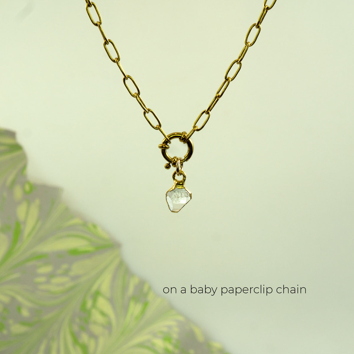 A gold paperclip chain necklace with a small gold clasp and a clear faceted herkimer diamond stone pendant