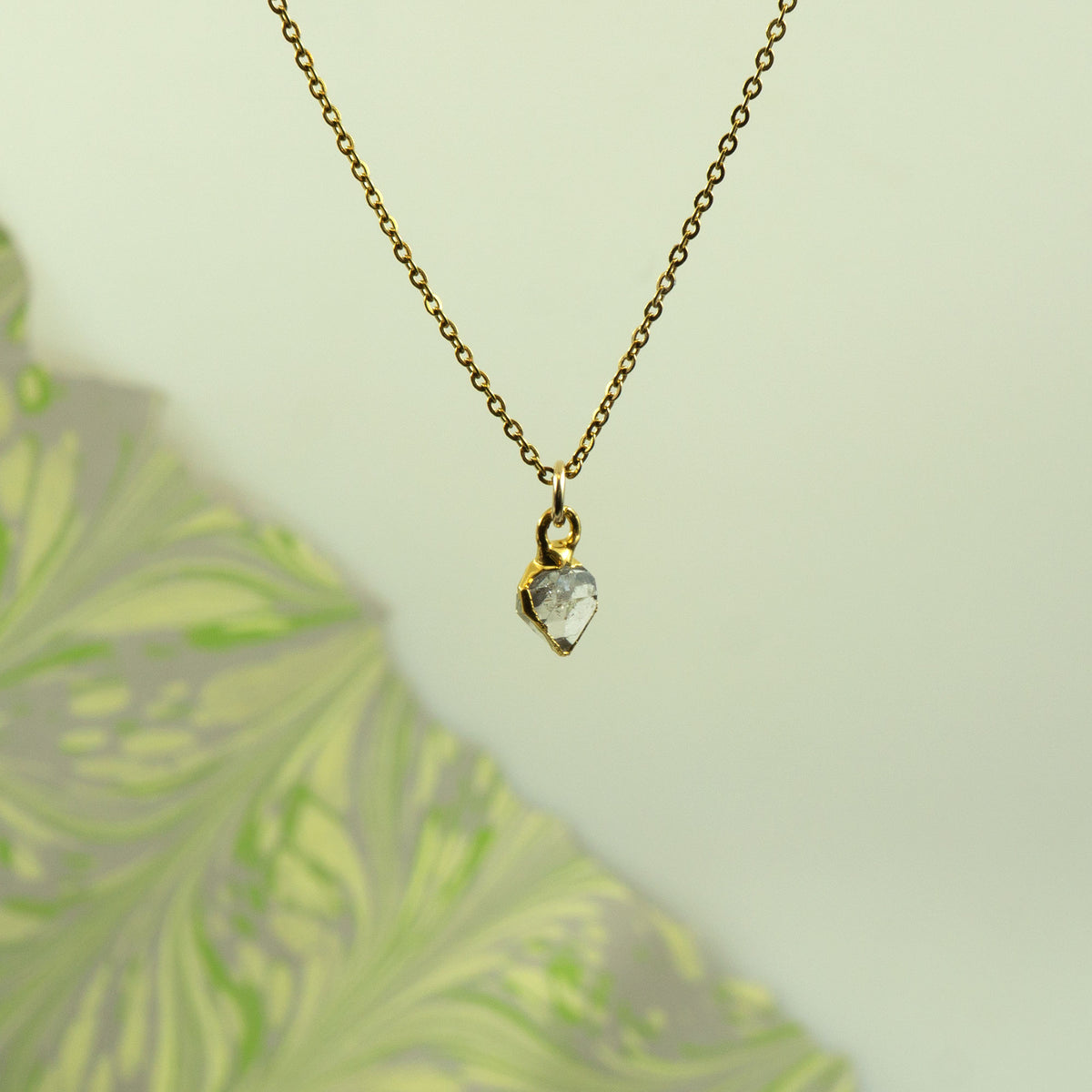 A gold chain necklace with a small gold heart-shaped bezel holding a clear faceted herkimer diamond stone
