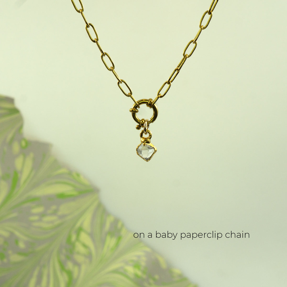 A gold paperclip chain necklace with a small gold clasp and a clear heart-shaped herkimer diamond pendant.