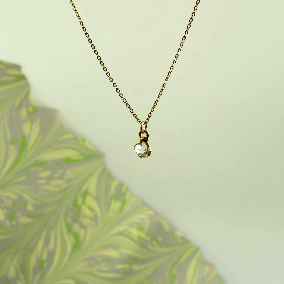 A delicate gold chain necklace with a small gold bail holding a clear heart-shaped herkimer diamond pendant