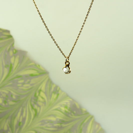 A delicate gold chain necklace with a small gold bail holding a clear heart-shaped herkimer diamond pendant
