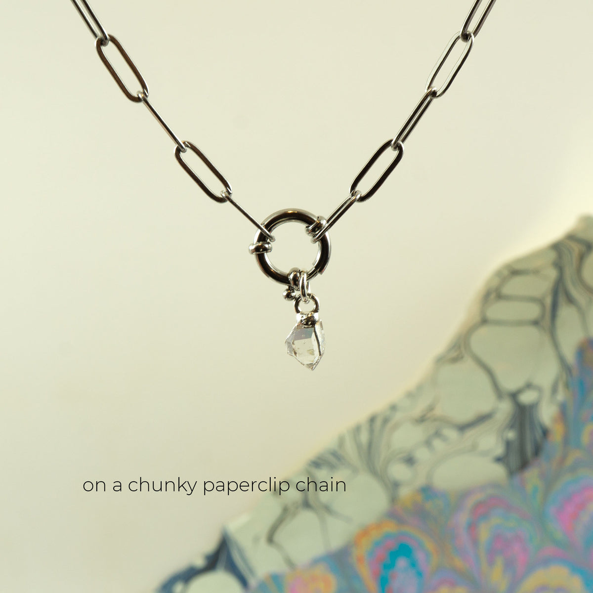 A silver paperclip chain necklace with a central ring and a small clear faceted herkimer diamond pendant