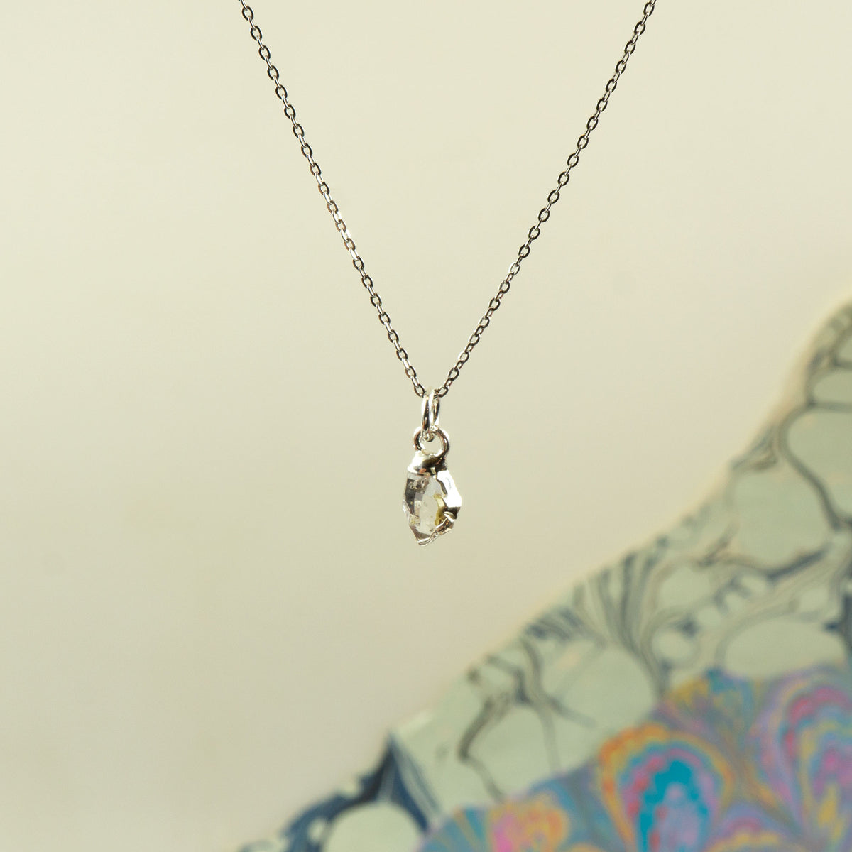 A delicate silver chain necklace with a small marquise-cut clear herkimer diamond pendant