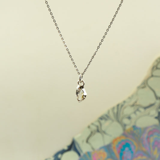 A delicate silver chain necklace with a small marquise-cut clear herkimer diamond pendant
