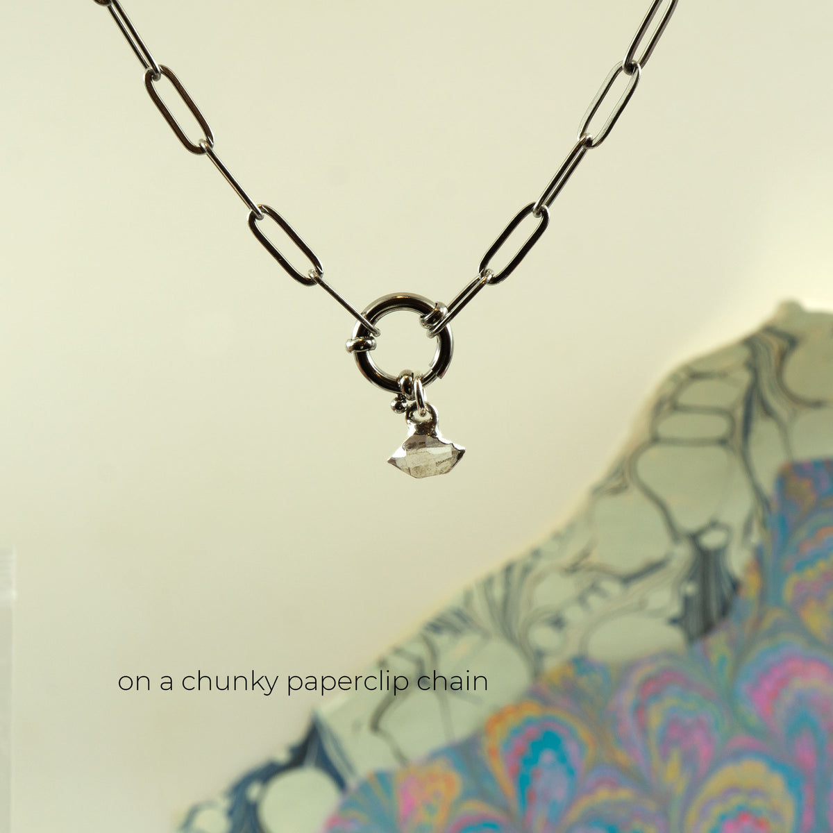 A silver paperclip chain necklace with a small clear Herkimer Diamond crystal pendant