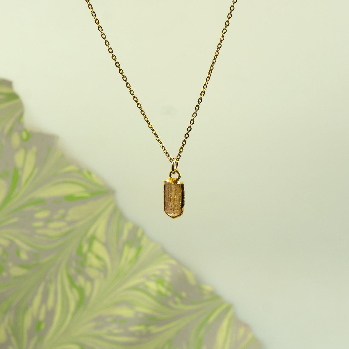 A gold chain necklace with a small rectangular Imperial Topaz pendant.