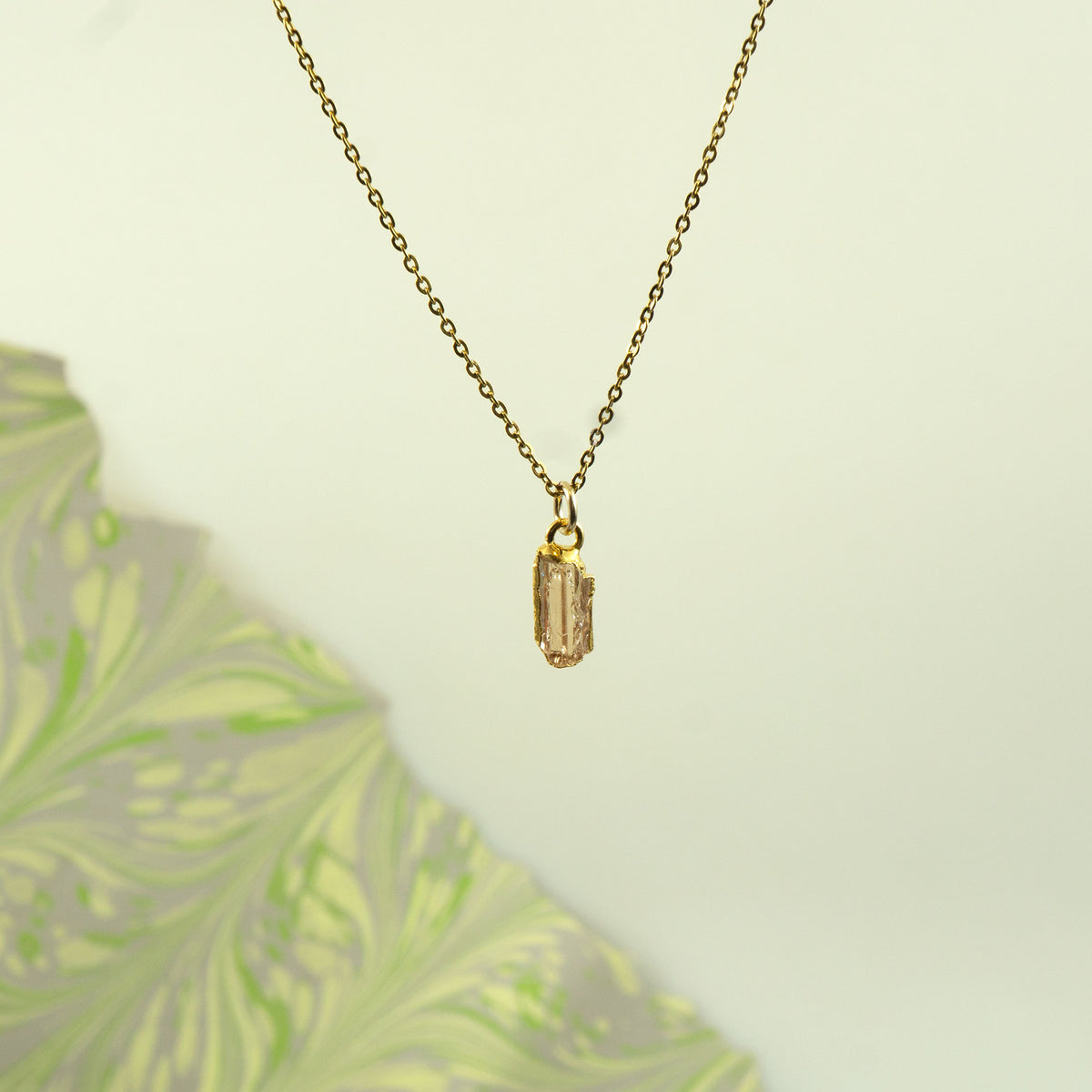 A delicate gold chain necklace with a small rectangular imperial topaz gemstone pendant.