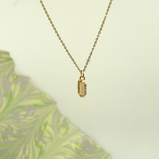 A delicate gold chain necklace with a small rectangular imperial topaz gemstone pendant.