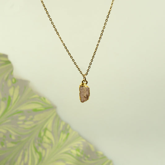 A gold chain necklace with a raw, irregular orange - peach Imperial Topaz crystal pendant.