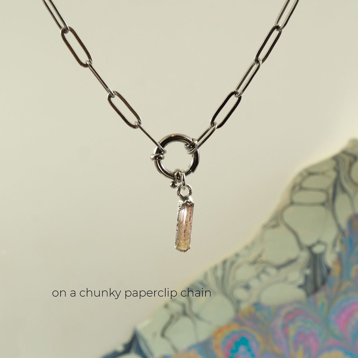 A silver-toned paperclip chain necklace with a ring clasp and a small dangling Imperial Topaz crystal charm,