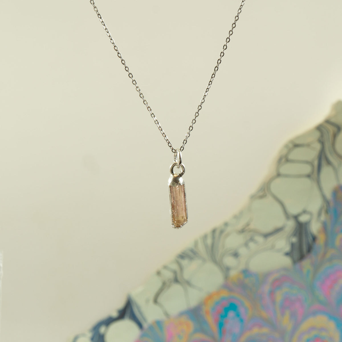 A delicate silver chain necklace with a small cylindrical Imperial Topaz crystal pendant.
