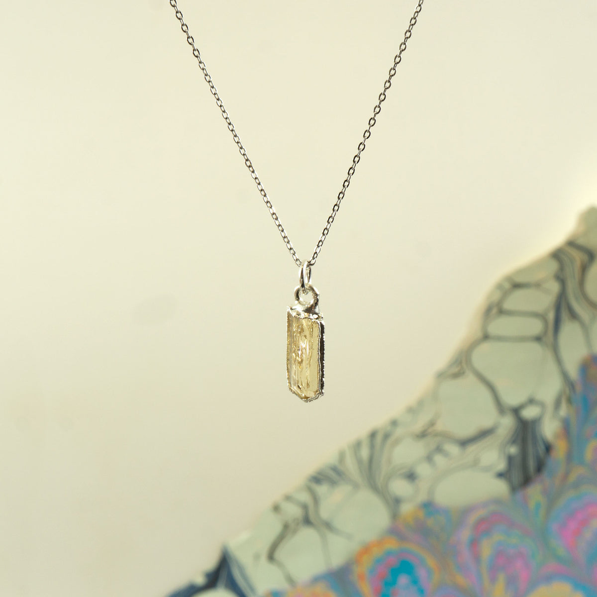 A delicate silver chain necklace with a small rectangular faceted Imperial Topaz crystal pendant.