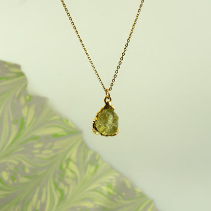 A gold chain necklace with a raw, irregular-cut Lemon Quartz gemstone pendant