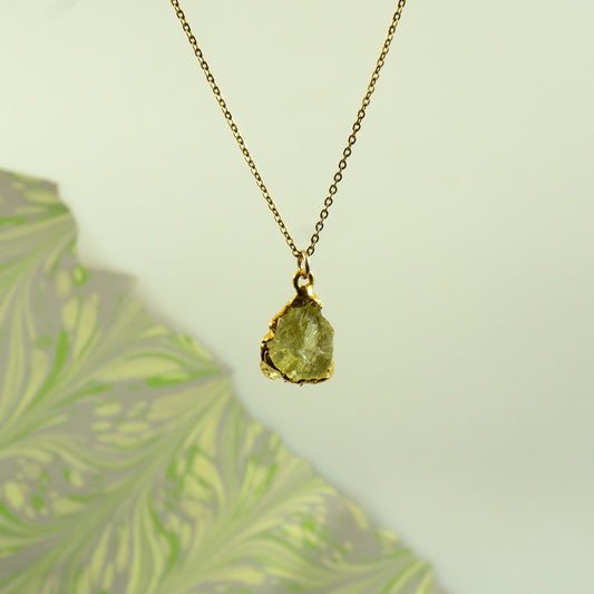 A gold chain necklace with a raw, irregular-cut Lemon Quartz gemstone pendant