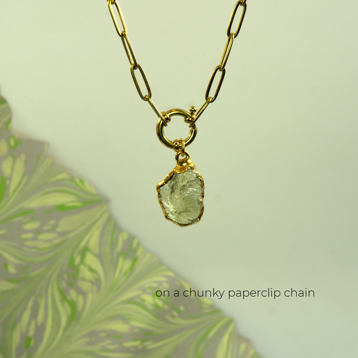 A gold necklace with a chunky paperclip chain and a raw, irregular-cut pale green Lemon Quartz gemstone pendant