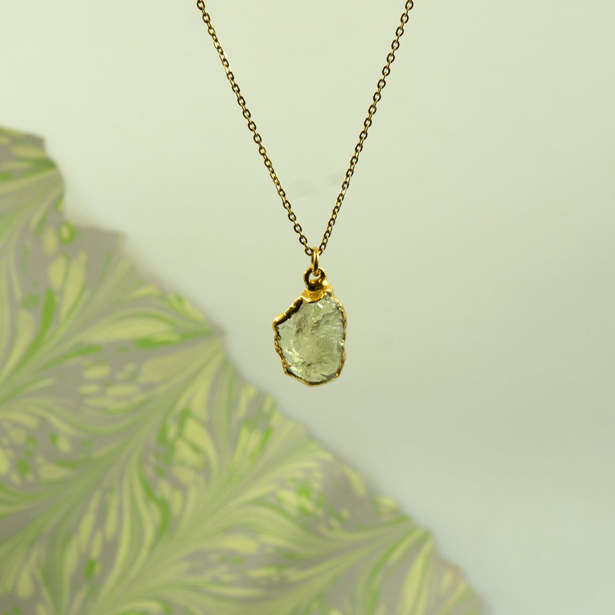 A gold chain necklace with a raw, irregular-cut pale green Lemon Quartz gemstone pendant