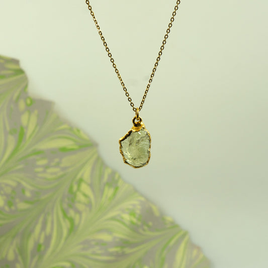 A gold chain necklace with a raw, irregular-cut pale green Lemon Quartz gemstone pendant