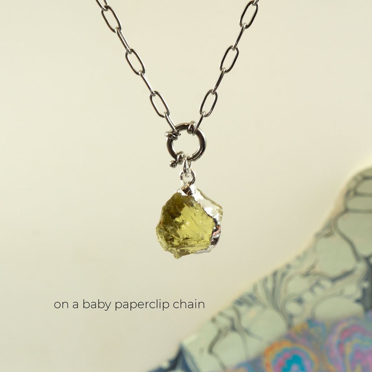 A silver paperclip chain necklace with a small ring clasp holding a rough, irregular yellow-green Lemon Quartz gemstone pendant