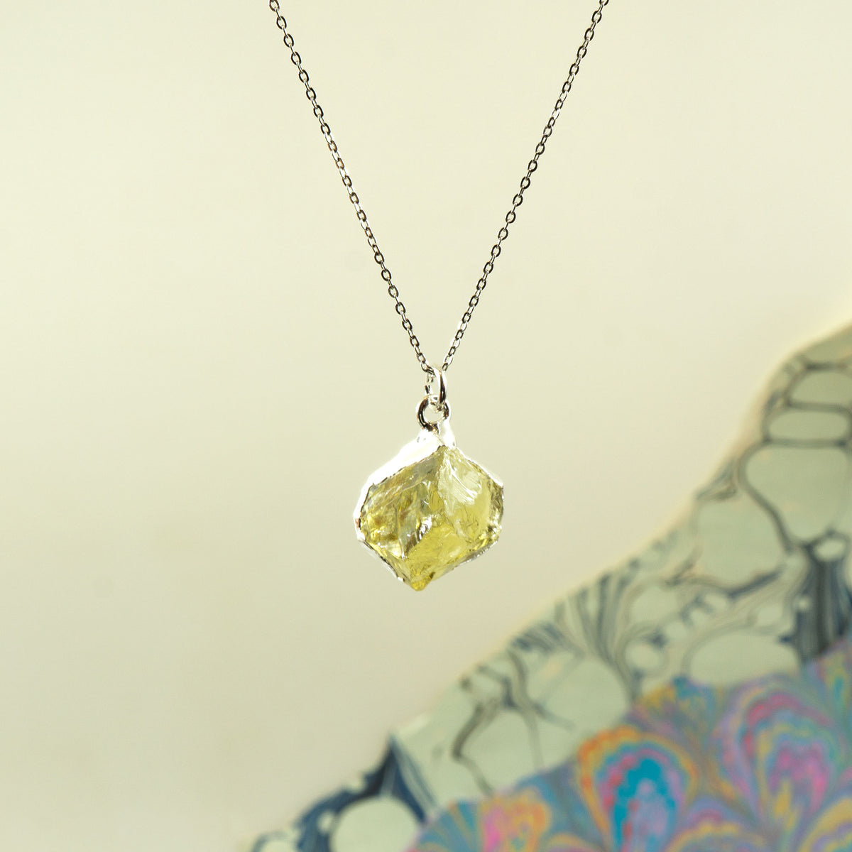 A silver chain necklace with a raw, irregular faceted Lemon Quartz gemstone pendant