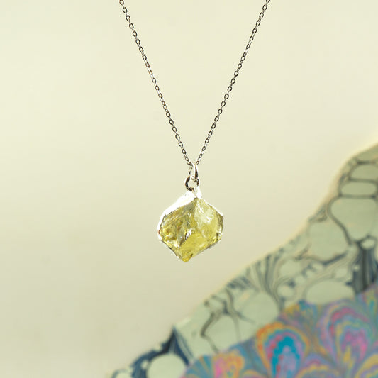 A silver chain necklace with a raw, irregular faceted Lemon Quartz gemstone pendant