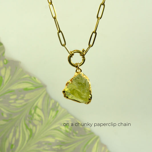 A gold necklace with a chunky paperclip chain and a raw, irregular lemon quartz, yellow-green gemstone pendant
