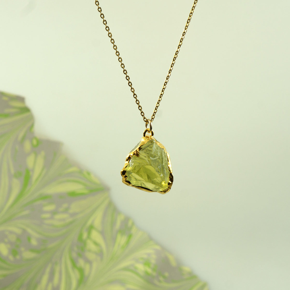 A gold chain necklace with a raw, irregular-cut lemon quartz gemstone pendant