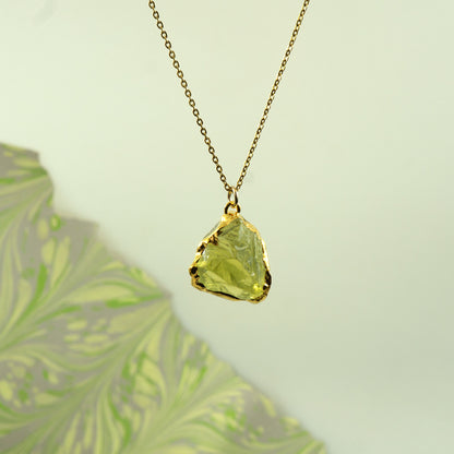 A gold chain necklace with a raw, irregular-cut lemon quartz gemstone pendant