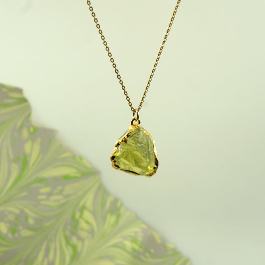 A gold chain necklace with a raw, irregular-cut lemon quartz gemstone pendant