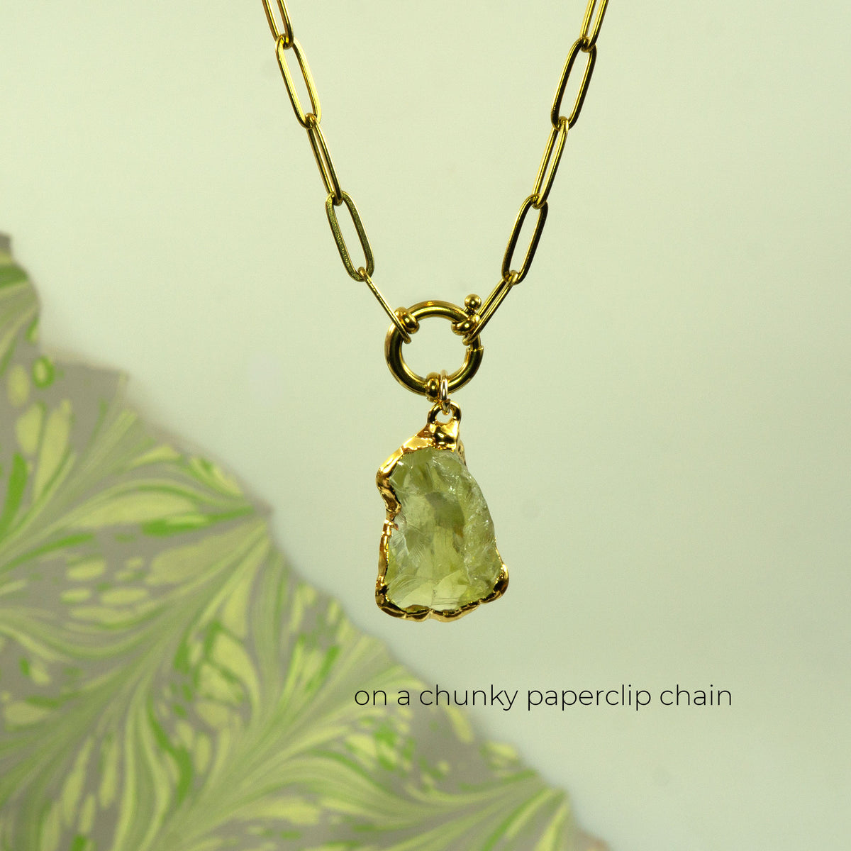 A gold necklace with a chunky paperclip chain and a raw, rough-cut pale green Lemon Quartz gemstone pendant,