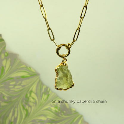 A gold necklace with a chunky paperclip chain and a raw, rough-cut pale green Lemon Quartz gemstone pendant,