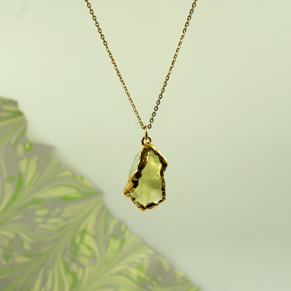 A gold chain necklace with a raw, irregular-cut light green Lemon Quartz gemstone pendant