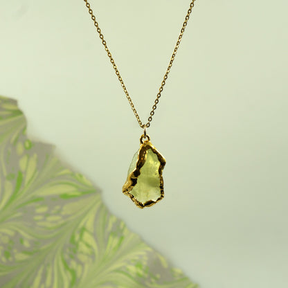A gold chain necklace with a raw, irregular-cut light green Lemon Quartz gemstone pendant