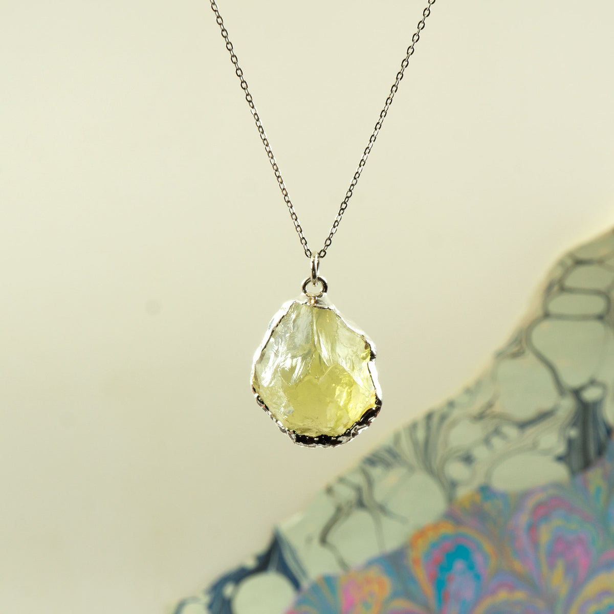 A silver chain necklace with a raw, irregular-cut pale yellow Lemon Quartz gemstone pendant.