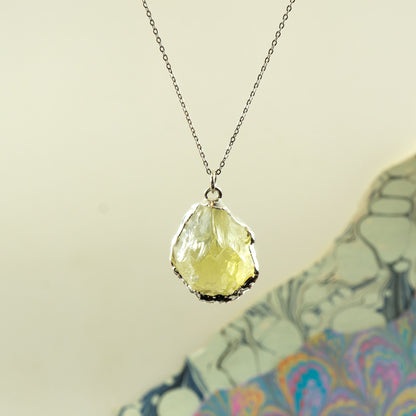 A silver chain necklace with a raw, irregular-cut pale yellow Lemon Quartz gemstone pendant.
