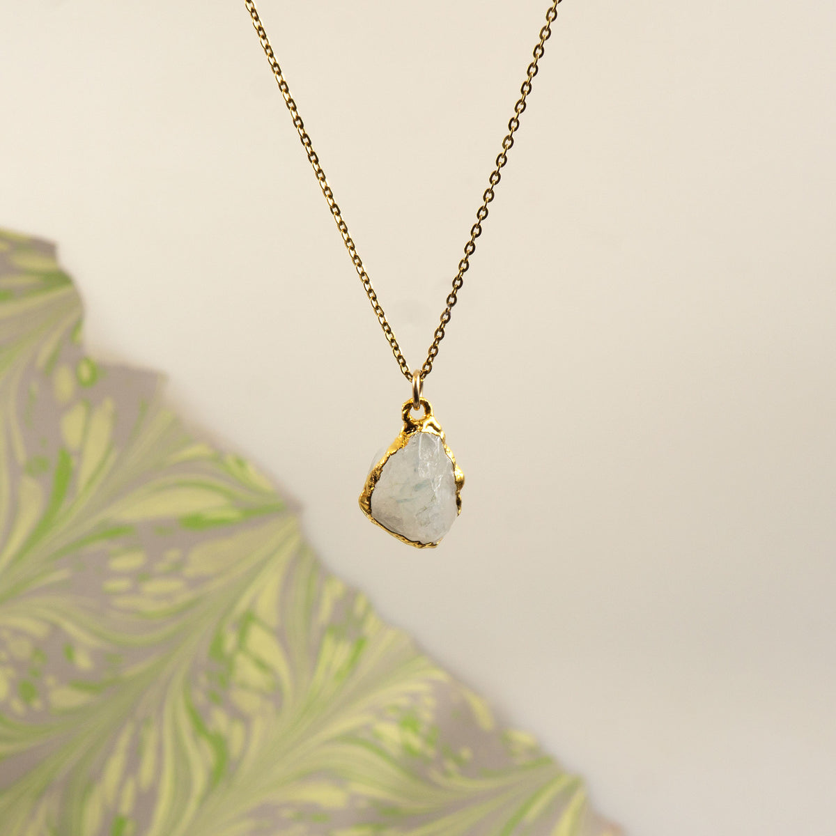 A gold chain necklace with a raw, irregular-shaped white stone pendant,