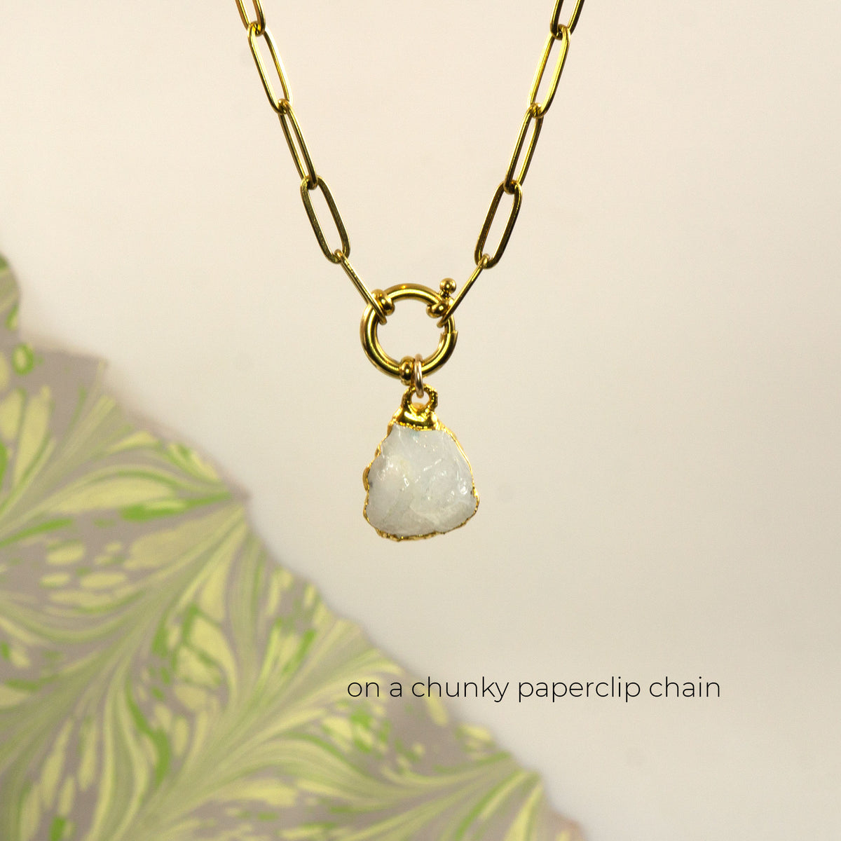 A gold paperclip chain necklace with a small gold ring connector and a raw, irregular white Rainbow Moonstone stone pendant