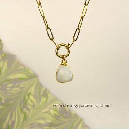 A gold paperclip chain necklace with a small gold ring connector and a raw, irregular white Rainbow Moonstone stone pendant