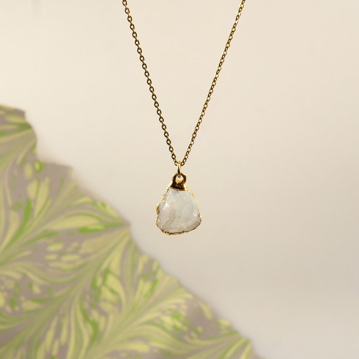 A delicate gold chain necklace with a raw, irregular-cut white Rainbow Moonstone stone pendant