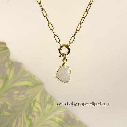 A gold paperclip chain necklace with a small gold ring clasp holding a raw, irregular white Rainbow Moonstone pendant